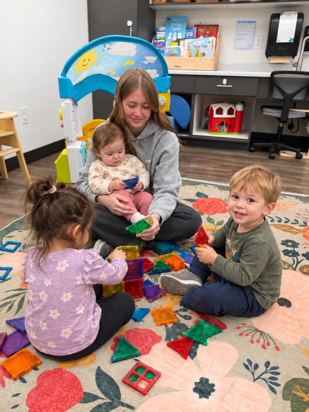 A teacher playing with little ones on the rug